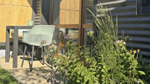 Een modern buitenzitje met een tafel en stoelen, omgeven door groen en bloemen.