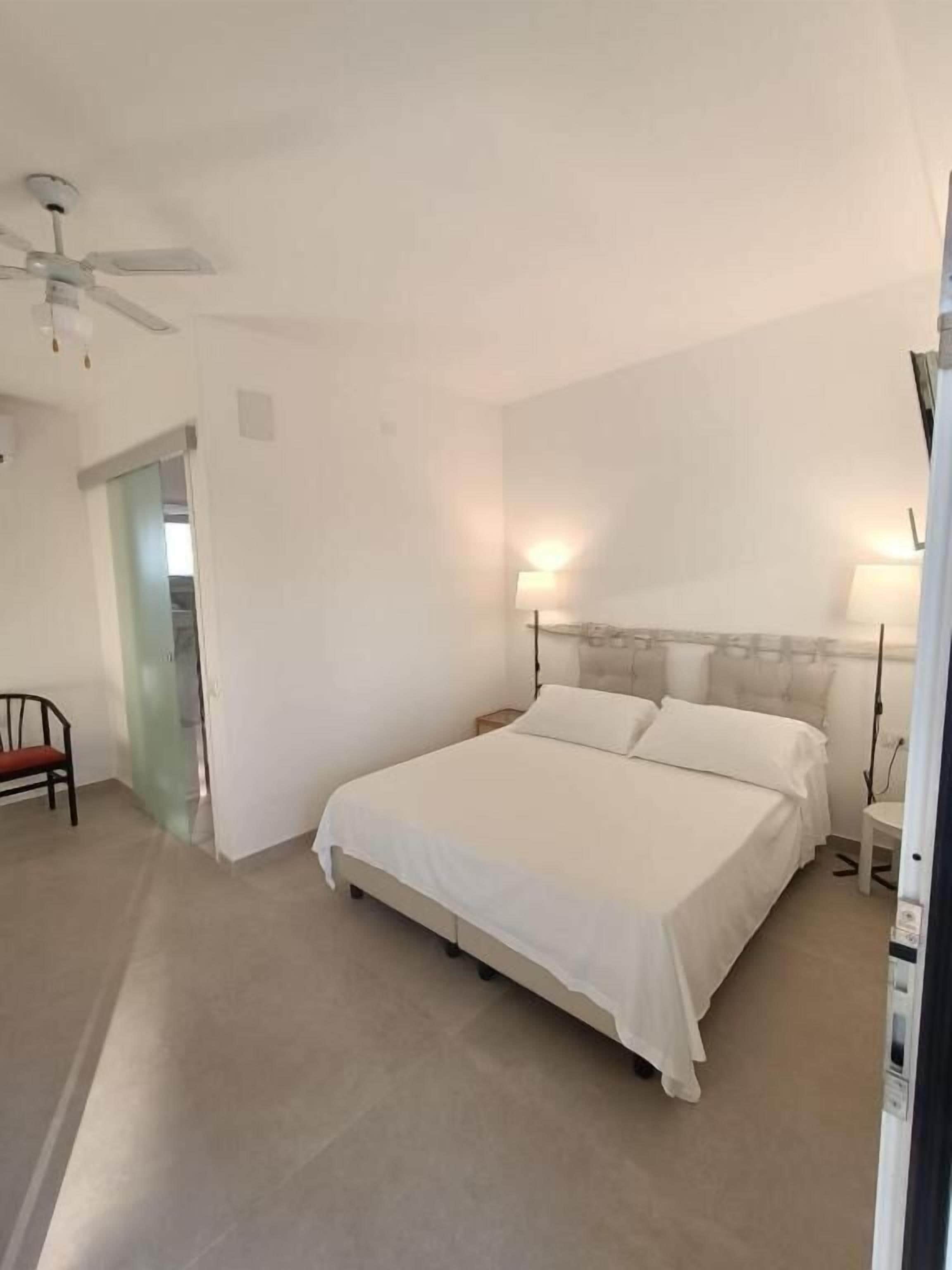 A spacious bedroom with a large bed, bedside lamps, a ceiling fan, and a chair.
