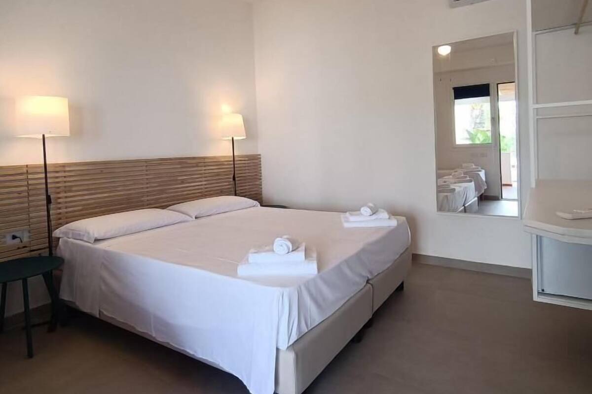 A modern hotel room with a large bed, two bedside lamps, a wooden headboard, and a built-in wardrobe.