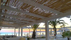 Un espacio al aire libre con mesas y sillas, vista al mar y palmeras.