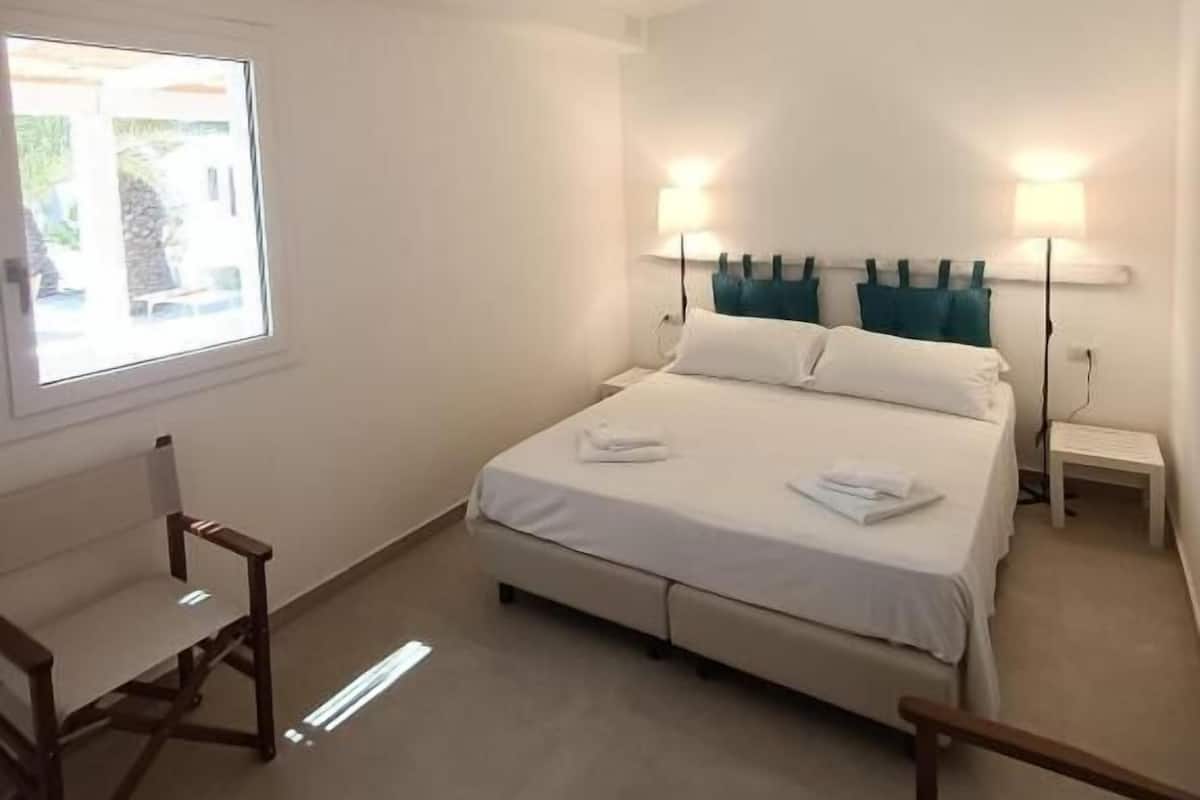 A bedroom with a bed, two bedside lamps, a ceiling fan, and a window.