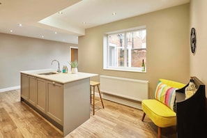 A modern kitchen with a central island, a window with a view of the outside, and a yellow sofa in the living area. - Host & Stay | Crescent House (Morpeth)