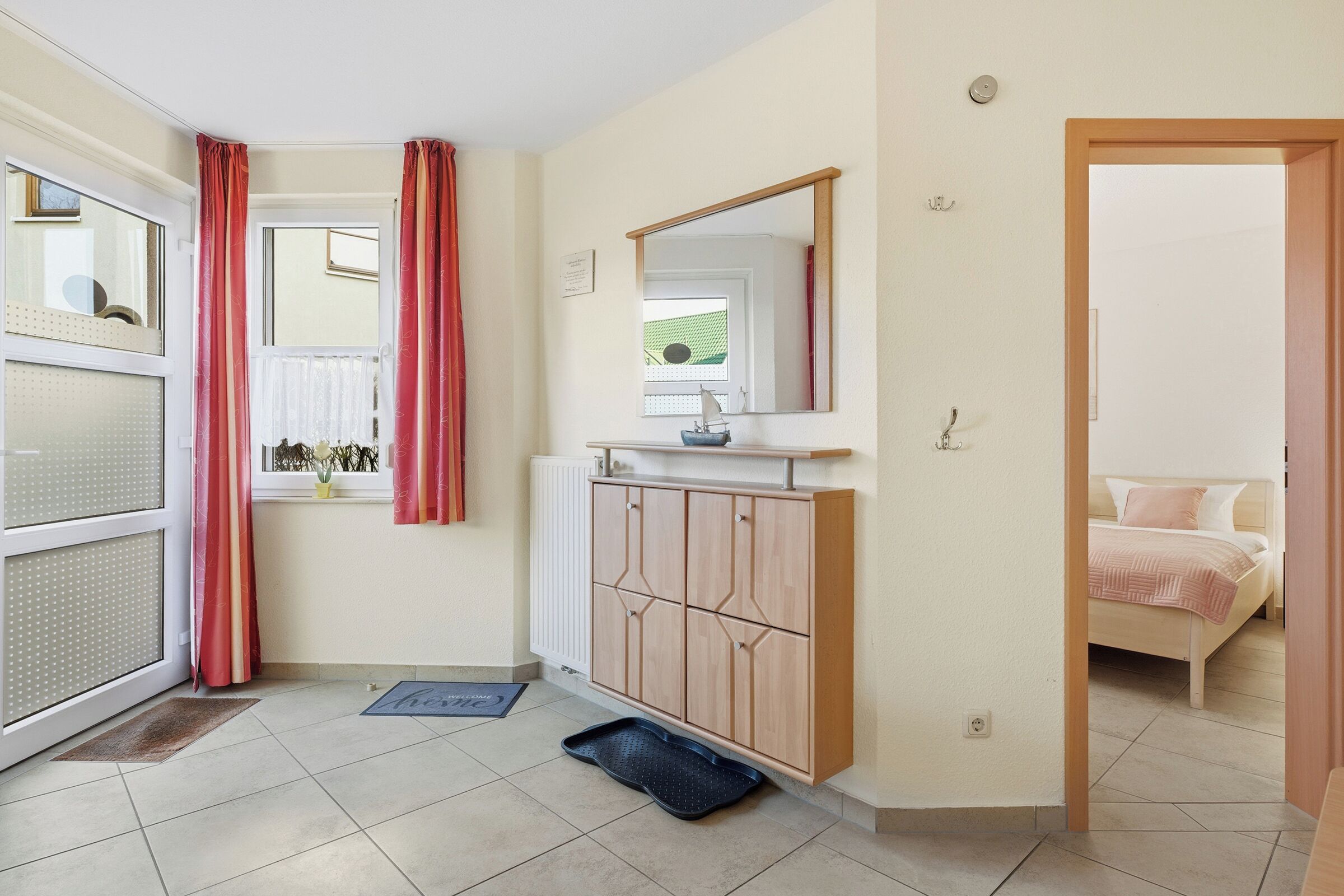 Una camera d'albergo con un letto, un armadio in legno, una finestra con tende, uno specchio e una porta che dà su un'altra stanza.