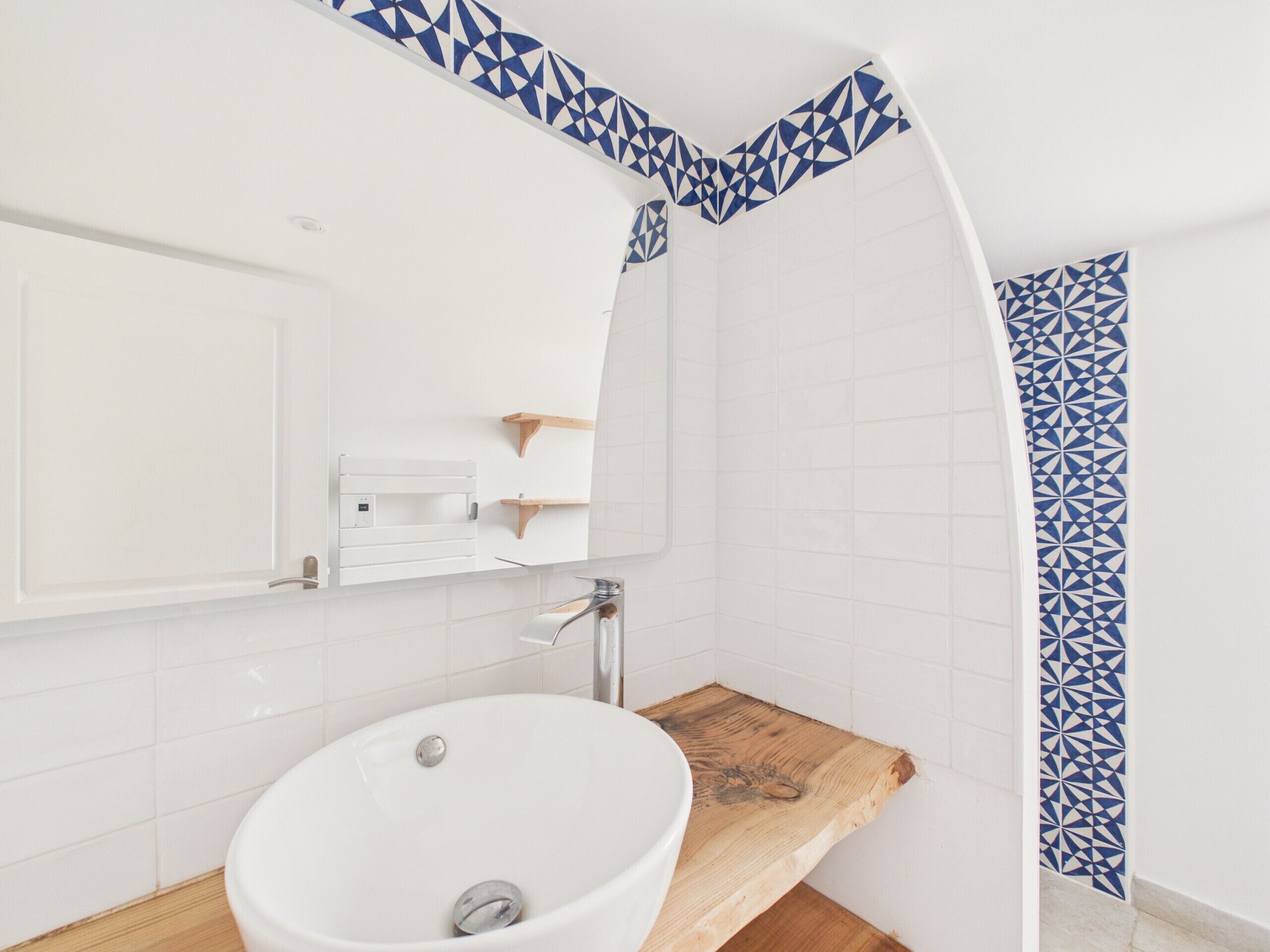 Um banheiro com pia branca, prateleira de madeira e design de azulejos geométricos azuis na parede.