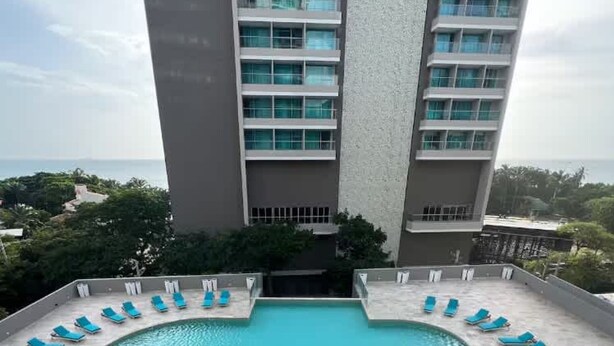 Une piscine sur le toit, dotée de chaises longues bleues et offrant une vue sur un grand immeuble à multiples balcons.
