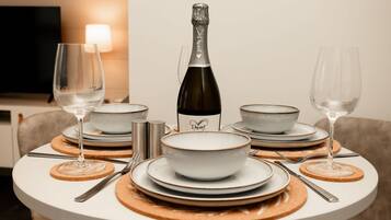 A dining table set with white plates, bowls, and cutlery, a bottle of champagne, and two glasses.