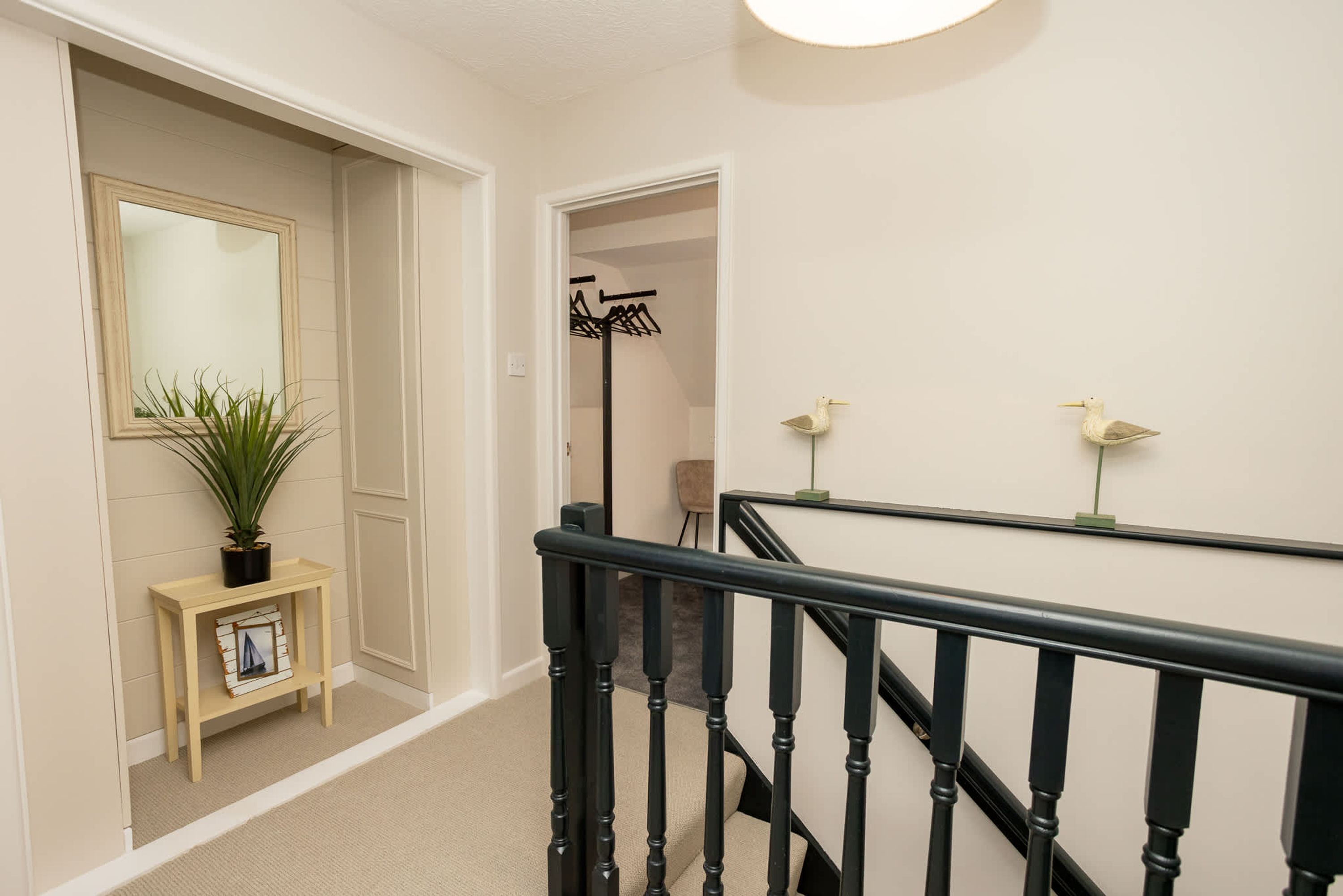 A hallway with a staircase, a small table with a plant, and a coat rack in the background.