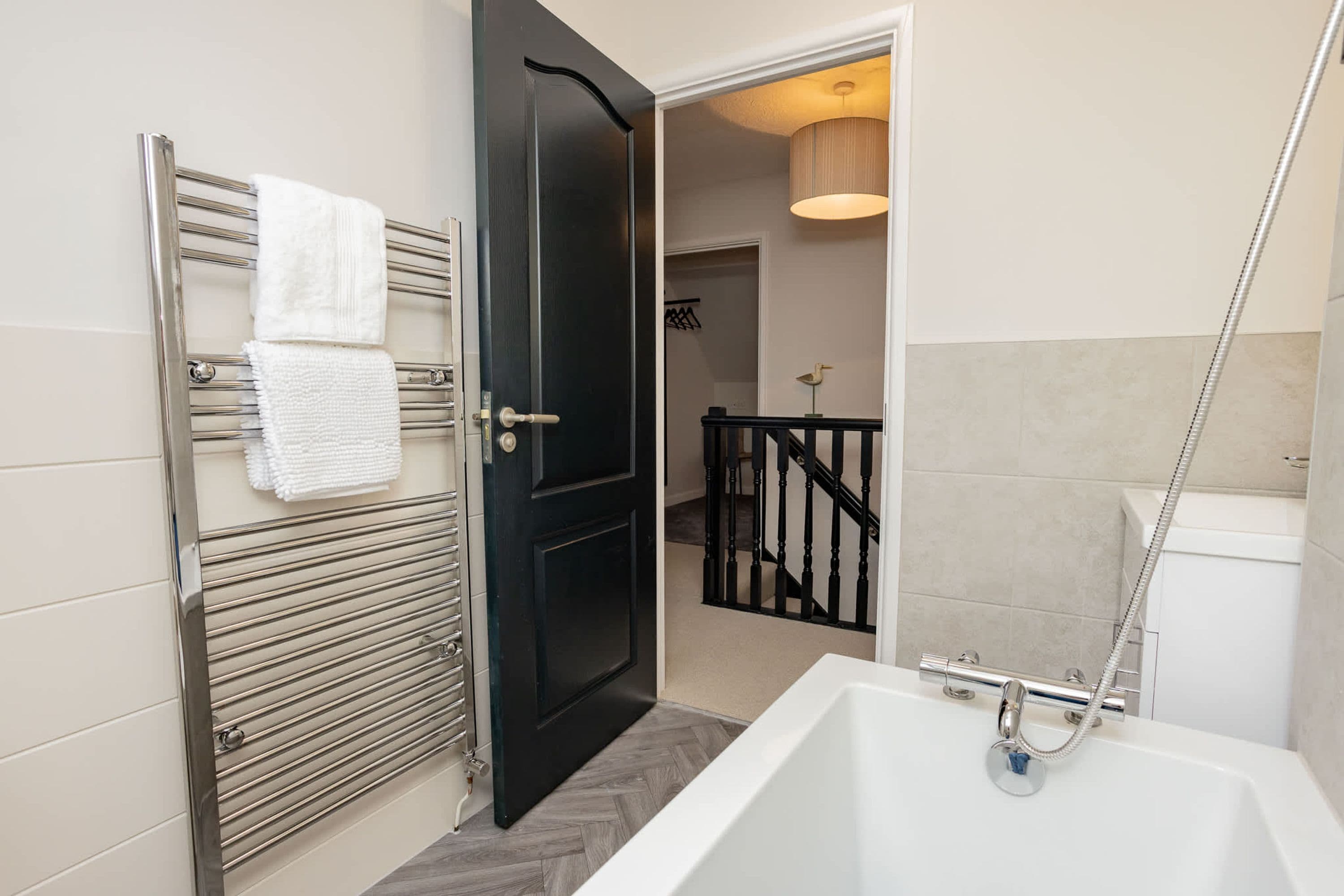 A modern bathroom with a white bathtub, a black door, and a metal towel rack with white towels.