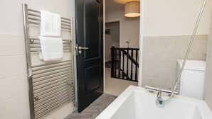 Un baño moderno con una bañera blanca, una puerta negra y un perchero metálico con toallas blancas.
