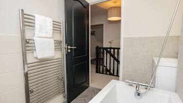 A modern bathroom with a white bathtub, a black door, and a metal towel rack with white towels.