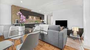Ein modernes Wohnzimmer mit grauem Sofa, einem Glastisch und einem Fernseher.