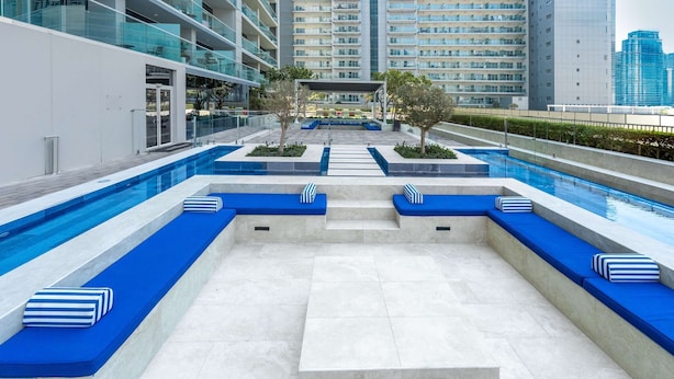 Un área de piscina moderna al aire libre con asientos azules y vista despejada de los edificios circundantes.