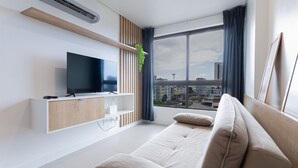 A modern living room with a flat-screen TV, a sofa, and a large window with a city view. - Parque Shopping #304 - Exclusive Apto by Carpediem (Recife)