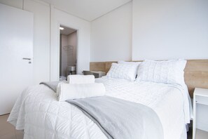 Une chambre à coucher moderne avec un grand lit, du linge de lit blanc, une tête de lit en bois et une table de chevet blanche.
