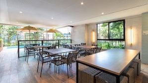 A spacious outdoor dining area with multiple tables and chairs, large umbrellas, and a view of greenery. - Parque Shopping #304 - Exclusive Apto by Carpediem (Recife)