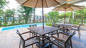 A poolside area with wooden tables and chairs, umbrellas, and a view of the pool and greenery. - Parque Shopping #304 - Exclusive Apto by Carpediem (Recife)