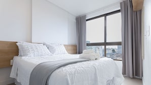 A modern hotel room with a large bed, a wooden headboard, and a city view through the window. - Parque Shopping #304 - Exclusive Apto by Carpediem (Recife)