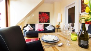 Un coin repas avec une table dressée pour deux personnes, un canapé en arrière-plan et un tableau représentant une fleur rouge accroché au mur.