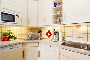 A kitchen with white cabinets, a microwave, a sink, and a coffee maker. - Comfortable vacation apartment Strandperle 1st floor/DG with balcony in Wenningstedt (Wenningstedt)