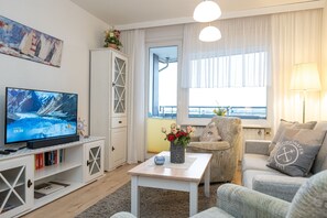 A living room with a television, a white cabinet, a sofa, a coffee table, and a window with curtains. - Comfortable vacation apartment with balcony in the heart of Westerland (Westerland)