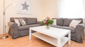 Een woonkamer met twee grijze banken, een witte salontafel en een vloerlamp.