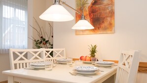 Een eetruimte met een witte tafel gedekt voor vier personen, twee hanglampen en een fruitschaal op tafel.