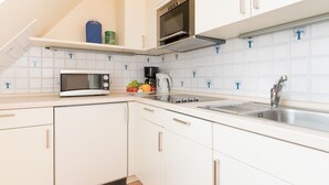 Een moderne keuken met witte kastjes, een magnetron, een waterkoker en een spoelbak.