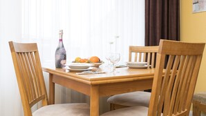 A wooden dining table with four chairs, a bottle of champagne, a bowl of fruit, and a wine glass. - Hyggelige vacation apartment with swimming pool and sauna in Haus Ornum in Westerland (Westerland)