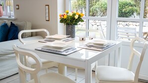 Een eetgedeelte met een witte tafel gedekt voor vier personen, omringd door witte stoelen. Op de tafel staat een vaas met gele en witte bloemen.