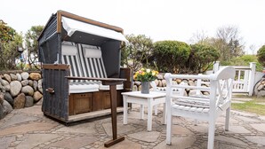 Een gezellig buiten zitgedeelte met een beklede bank, een kleine tafel met een bloemenvaas, en een witte stoel.