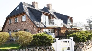 Een herenhuis met twee verdiepingen, een steile dakschild, een balkon en een stenen muur met een witte hekwerkhek.