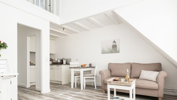 En modern lägenhet i loftstil med ett matområde, ett litet kök och ett vardagsrum med soffa och soffbord.