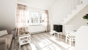 Ett ljust vardagsrum med en vit soffa, ett soffbord, en tv och en trappa.