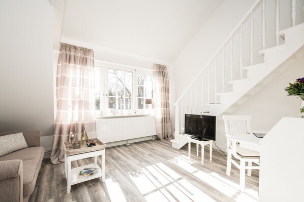A bright living room with a white sofa, a coffee table, a TV, and a staircase. - Comfortable vacation apartment in Westerland with modern furnishings and parking space (Westerland)