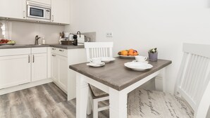 Ett modernt kök med vita köksskåp, en mikrovågsugn och en matplats med ett träbord och vita stolar.