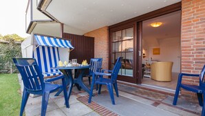 An outdoor patio with a table and blue chairs, a striped awning, and a brick wall. - Comfortable vacation apartment with garden and terrace (Wenningstedt)