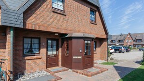 A brick house with a garage, a bicycle, and parked cars. - Comfortable vacation apartment with garden and terrace (Wenningstedt)