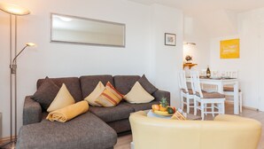 A modern living room with a grey sectional sofa, a yellow armchair, and a dining area with a white table and chairs. - Comfortable vacation apartment with garden and terrace (Wenningstedt)