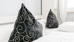 A bed with black pillows featuring white swirls, a white headboard, and a white wall in the background. - Modern vacation apartment with sauna, solarium and heated indoor pool in Westerland (Westerland)
