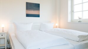 Una habitació d'hotel amb dos llits individuals, una taula de nit amb una làmpada, una finestra que dona al cel i una obra d'art penjada a la paret.