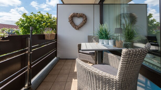 Ein Balkon mit Korbmöbeln, einer herzförmigen Dekoration und Topfpflanzen.