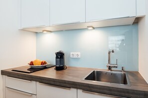 Eine moderne Küche mit Spüle aus Edelstahl, einer Kaffeemaschine und einer Obstschale auf der Arbeitsfläche.