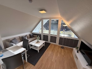 A modern loft bedroom with a sloped ceiling, a sofa, a dining table, and a TV. - Apartment 'Ostseestrand' with Balcony, Wi-Fi and Air Conditioning (Prerow)