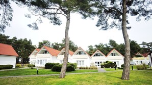 Une rangée de maisons blanches aux toits rouges, entourées de pelouses verdoyantes et d’arbres.