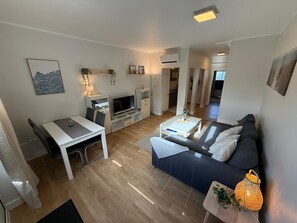 Una sala moderna con sofá, televisión, mesa de comedor y zona de cocina.