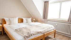 Un dormitorio con una cama de madera, ropa de cama blanca, un radiador y una ventana con cortinas.