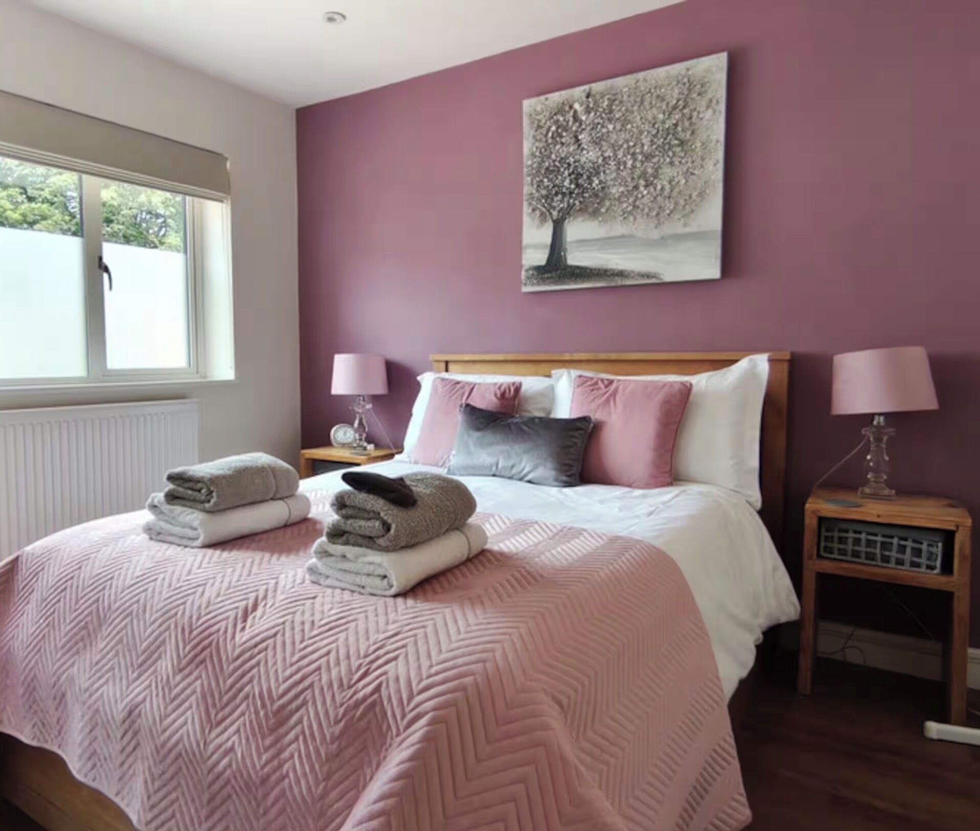 Une chambre à coucher avec un lit, deux tables de chevet, une fenêtre et un tableau au mur.