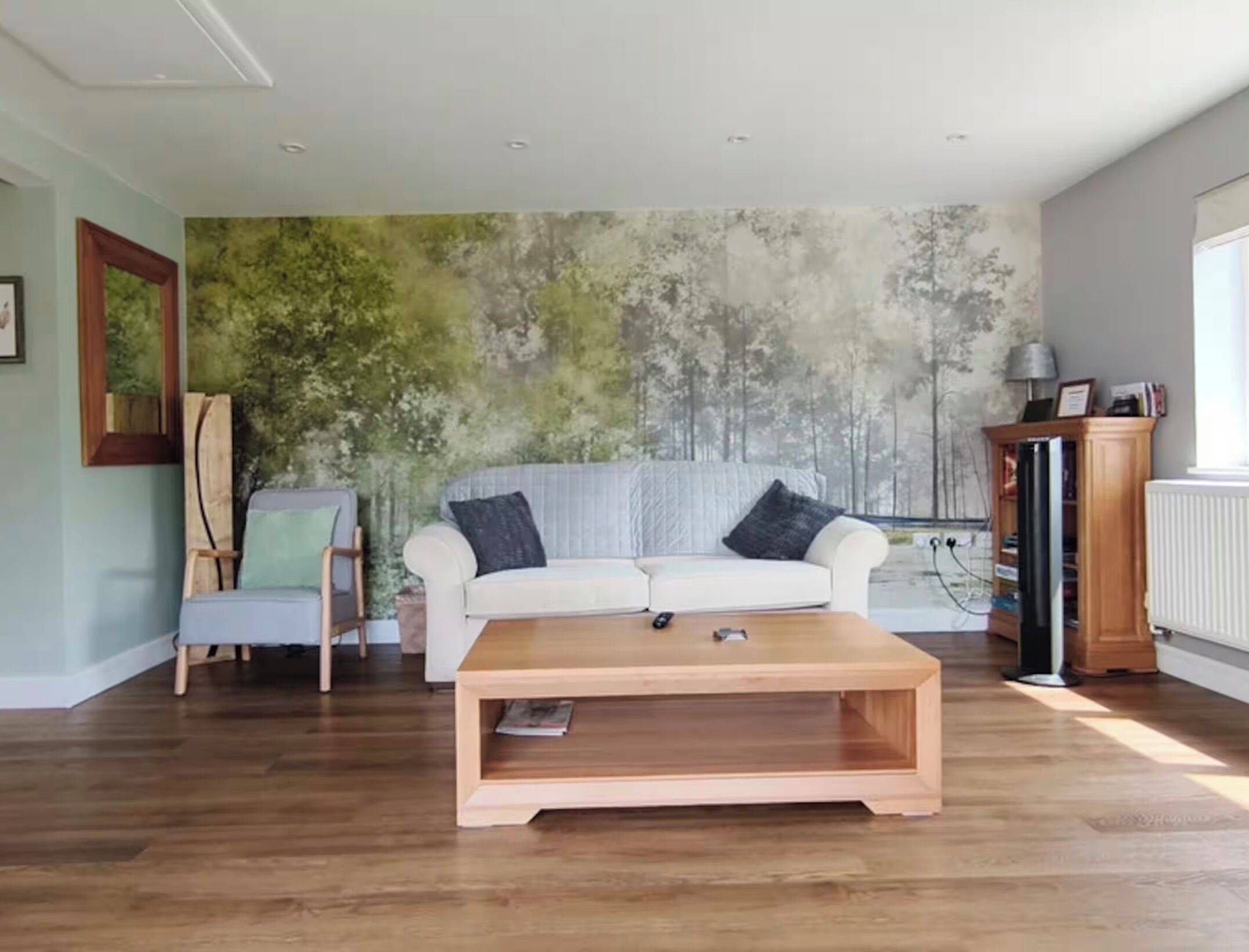 Un salon avec un canapé blanc, une table basse en bois, un tableau au mur et un radiateur.