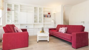 A living room with two red sofas, a white coffee table with a pineapple, and a white shelving unit against the wall. - Beautiful and modern house in Alt- Westerland (Westerland)