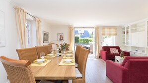 A dining area with a wooden table set for four, surrounded by wicker chairs. There is a red sofa and a white cabinet in the background. - Beautiful and modern house in Alt- Westerland (Westerland)